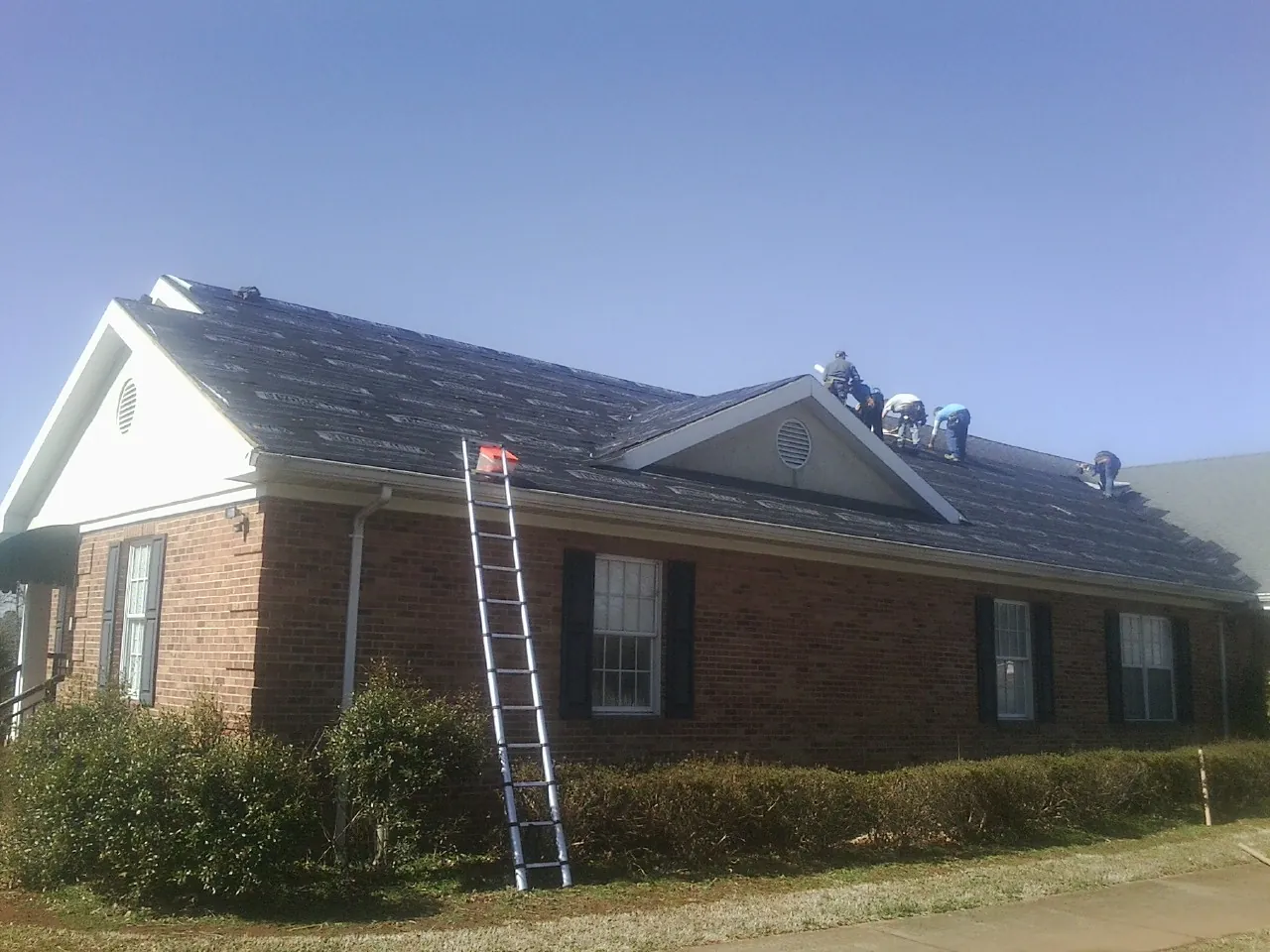 Crew tearing shingles off a brick ranch roof with a ladder set — Emergency Roof Repair work by our crew in Calhoun