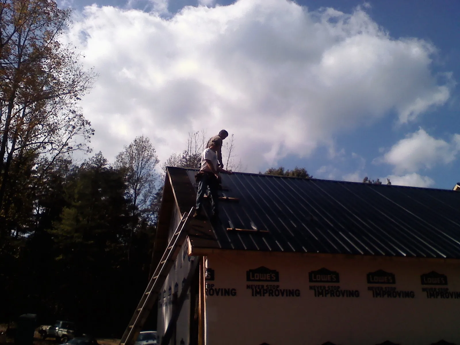 Roofer fastening dark metal panels high against a cloudy sky, from a Roof Inspection job in Calhoun